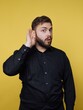 © bodnarphoto - Man with a surprised expression listening closely against a vibrant yellow background on a bright day