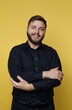 © bodnarphoto - Young man with a friendly smile poses confidently against a bright yellow background while wearing a stylish black shirt