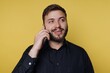 © bodnarphoto - Smiling man enjoying a cheerful phone conversation against a vibrant yellow backdrop