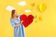© Pixel-Shot - Young woman with heart near decorated yellow wall. Valentine's Day celebration
