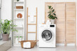 © Pixel-Shot - Modern washing machine with basket, shelving unit and dressing screen near white wall. Interior of home laundry room