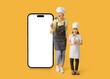 © Pixel-Shot - Happy female chef with her little daughter and big mobile phone with blank screen on yellow background
