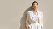 © NeuroCake - Asian woman in white suit and gold earrings. Stylish female model in blazer and trousers posing against beige backdrop. Business fashion concept