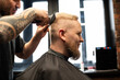 © Mariya Surmacheva - Barber cutting a man’s hair with clippers in a barbershop. Side profile of a male client with short haircut and beard, professional grooming service in a salon.