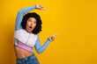 © deagreez - Young woman in stylish casual attire pointing in surprise at yellow background promoting interest and excitement