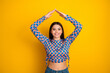 © deagreez - Young mixed race girl with bright yellow background wears a blue and orange checkered top and raises arms above her head for a vibrant fashion