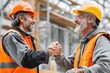 © anyatachka95 - Construction workers in safety gear exchanging a handshake at a building site.
