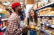 © unai - Diverse friends laughing while grocery shopping in supermarket aisle