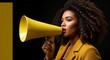 © Cleverson - A confident woman with curly hair holding a yellow megaphone to her mouth in a dark room.