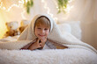 © Tomsickova - Little cute preschool boy, holding cute teddy bear, hiding under blanketl, playing at home in bedroom
