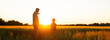 © Acronym - Farmer and his son in front of a sunset agricultural landscape. Man and a boy in a countryside field. Fatherhood, country life, farming and country lifestyle concept.