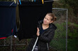 © Мар'ян Філь - A woman in a dark jacket hangs clothing on an outdoor clothesline beside a chain-link fence. A woman hangs out laundry in her free time, checking to see if shirts are washed properly