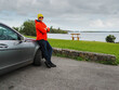 © mark_gusev - A tourist man in red jacket is standing by a car with picturesque lake in the background. The sky is cloudy and the water is calm. Travel and tourism. Calm and relaxing mood.