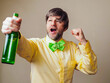 © mark_gusev - Excited man in his 40s or 50s in a yellow shirt and Irish green bow tie with shamrock is holding a bottle of beer. Light color background. Ireland sport fan. Male with grey beard and hair.