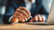 © estrel - Professional corporate closeup of a businessman at a laptop right hand raised higher above the desk and positioned clearly away from the laptop holding a white pen be