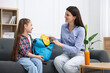 © New Africa - Mother and daughter packing backpack for school on sofa at home