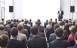 ©  TOFEL - A large audience attentively listening to a speaker at a conference or seminar in a spacious room