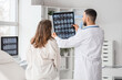 © Pixel-Shot - Male doctor showing MRI scan of head to woman in clinic, back view
