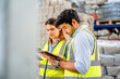 © sirichai - Diverse team of warehouse supervisors in safety vests using digital tablets to manage inventory and logistics in a large industrial printing facility storage area