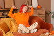 © Pixel-Shot - Young happy woman in headphones sitting on sofa and dancing at home