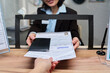 © pressmaster - Middle aged Caucasian woman handing approved visa application documents and passport to young adult Caucasian woman across counter at visa center, both women interacting during visa process