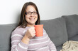 © amfer75 - Woman enjoying a hot cup of tea while relaxing on a comfortable sofa at home