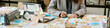 © AnnaStills - Caucasian woman working at cluttered desk covered with sticky notes, writing on paper beside open laptop, demonstrating busy business planning and organization process