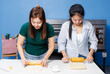 © Bangkok Click Studio - Two asian beautiful young woman cheerful bakers dough flour rolling pin on white table counter baking process mixing different ingredient making homemade bread sweet pastry in bakery kitchen teamwork.