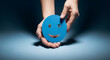 © alaa - Hands holding a blue smiling face symbol with cinematic spotlight on dark background