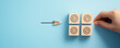 © Nan Shen - Goal achievement and business success concept with hand placing wooden block with target icon among check mark blocks on blue background for task management, strategy planning, and project milestone