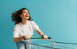 © Konstantin Yuganov - Happy Young Woman Enjoying Shopping with Cart on Blue Background ? Retail Lifestyle Concept