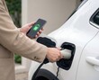 © Nadia - Man charging electric car with smartphone battery app and plug in cable at home