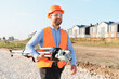 © Serhii - Surveyor geodetic engineer carrying total station equipment walking on construction site