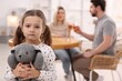 © New Africa - Alcohol addiction. Man and woman drinking whiskey at table indoors, focus on their sad daughter with toy bunny