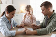 © New Africa - Family with Bible praying together at wooden table indoors