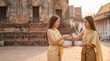 © 5 Grace Media - Two Thai women in traditional golden attire performing a water pouring ritual in a temple courtyard.