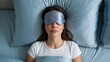 © TrendyImages - Young woman resting calmly in blue bedsheets wearing a silver sleeping eye mask overhead view