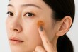 © AnilaStudio - 白い背景で、頬にできた茶色いシミを指で触るアジア人女性のクローズアップ。肌の悩みや美容医療、スキンケアのコンセプト。