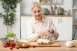 © Pixel-Shot - Mature happy woman grating cheese for delicious lasagna at table in kitchen