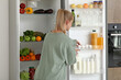© Pixel-Shot - Young woman choosing food in modern fridge at home
