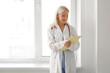 © Pixel-Shot - Female doctor writing in clipboard near window at hospital