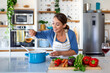 © Graphicroyalty - Woman cooking healthy meal in kitchen, pouring oil into pot with fresh vegetables on counter. Home chef preparing organic dinner. Healthy lifestyle, Mediterranean diet, and domestic cooking concept.