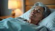 © Pete - Elderly woman rests peacefully in a hospital bed. Soft lamp light illuminates her serene face as she slepic deeply under a light blue blanket. She appears calm and undisturbed during her recovery.
