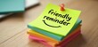 © Pete - Yellow sticky note with friendly reminder text and a face is pinned on a stack of colorful paper. The message serves as a cheerful prompt for tasks or appointments.