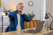 © Andrii Iemelianenko - Middle-aged businessman at home office suddenly clutches neck feeling sharp deep pain grimacing needing urgent relief. Freelancer guy at table stretches muscles massaging area hoping discomfort eases.