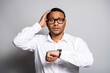 © deagreez - Confused businessman checks his watch in a white shirt standing before a plain studio background