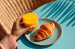 © aboutnuylove - croissant and orange juice in woman's hand on blue background