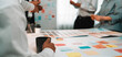 © InfiniteFlow - A diverse group of professionals engages in a lively brainstorming session, using colorful sticky notes to share ideas and enhance collaboration in a modern office setting. SACTR