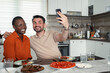 © Jelena - Happy multi-ethnic couple taking a selfie while having lunch in the kitchen