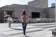 © wavebreak3 - Adult woman walking on terrace in pink hoodie, talking on phone, carrying backpack, crossbody bag